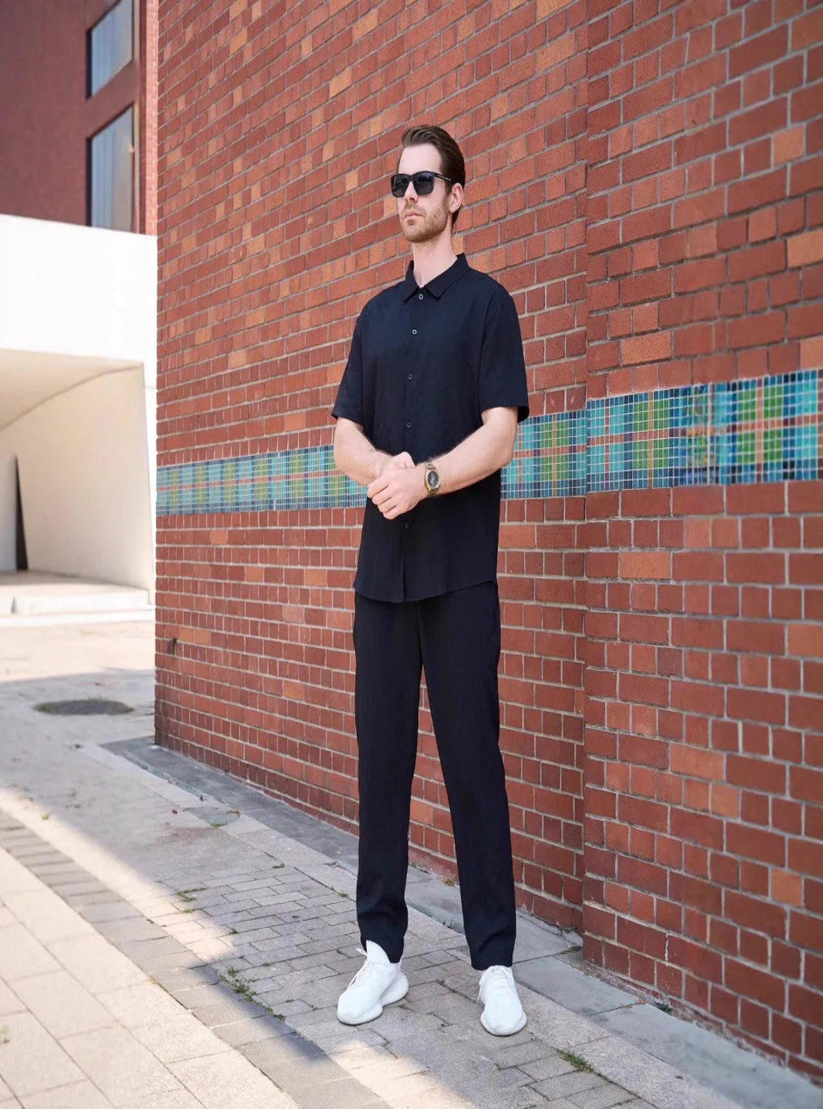Man in black outfit standing against a brick wall with a colorful stripe.