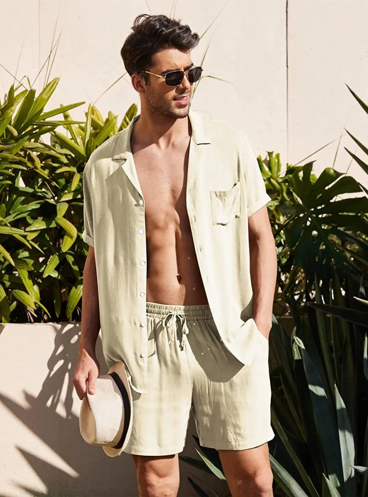 Man wearing a light-colored shirt and shorts outdoors with plants in the background