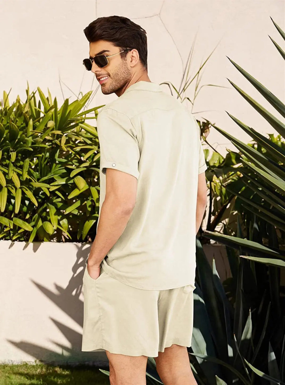 Man wearing a light-colored shirt and shorts standing outdoors with greenery in the background