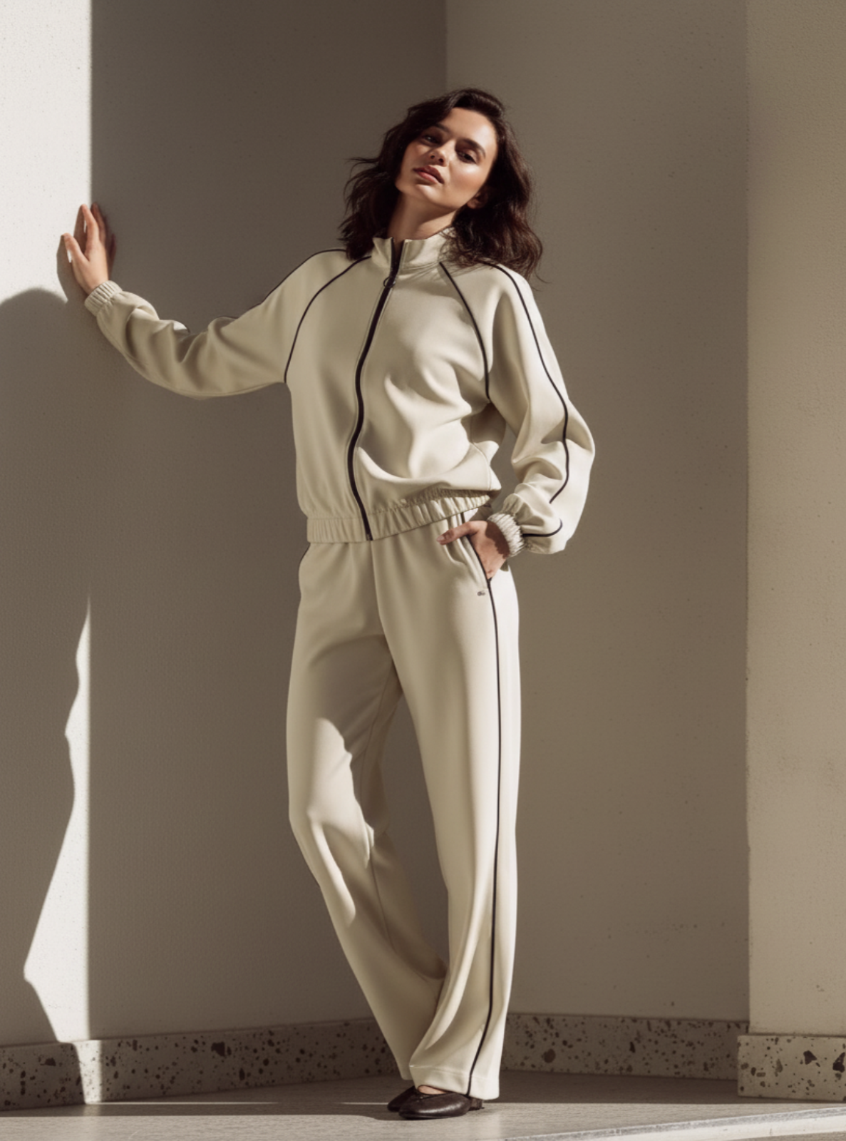 Woman wearing a beige tracksuit standing against a plain wall.