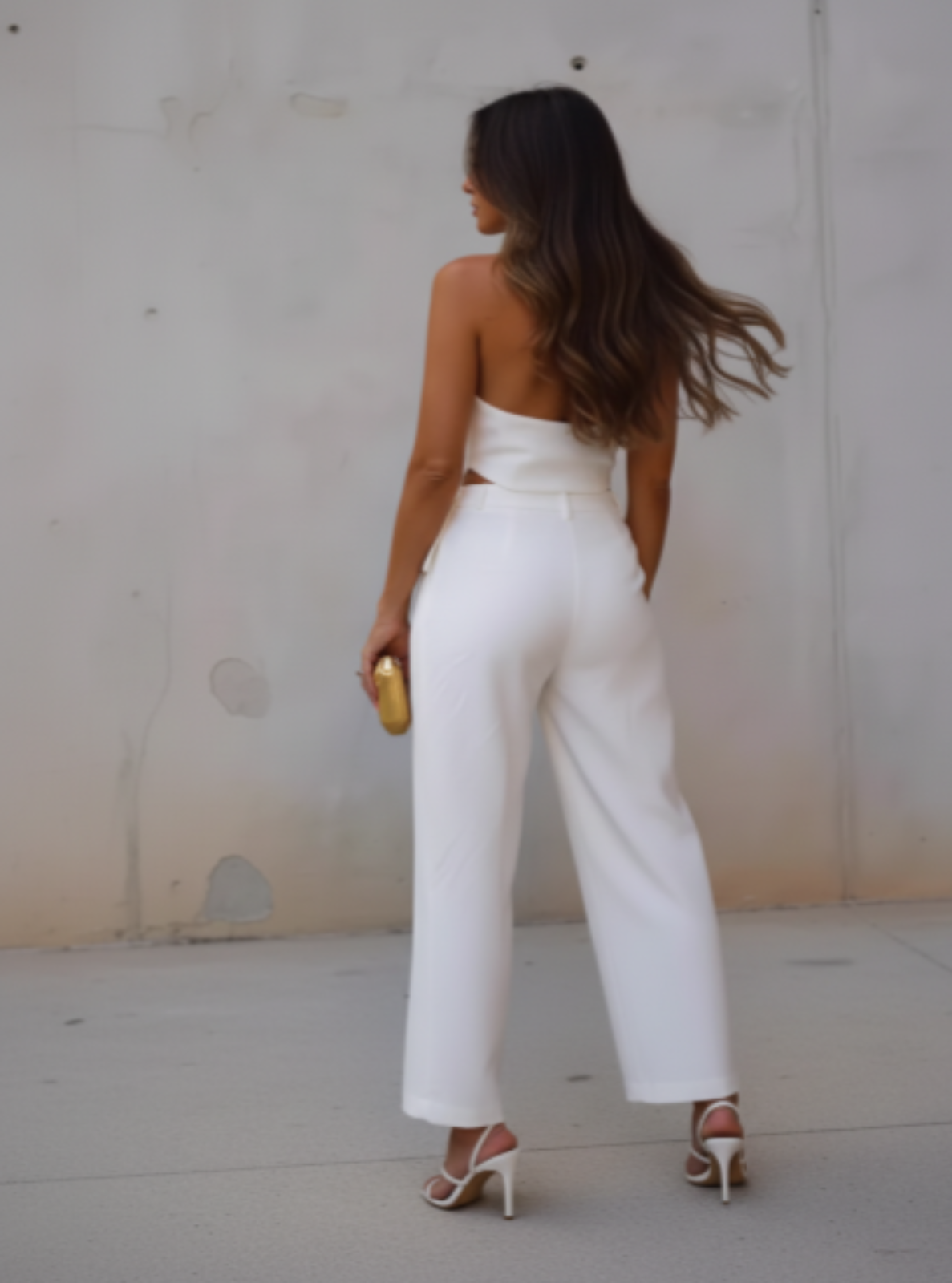 Woman in a white outfit standing against a plain wall.