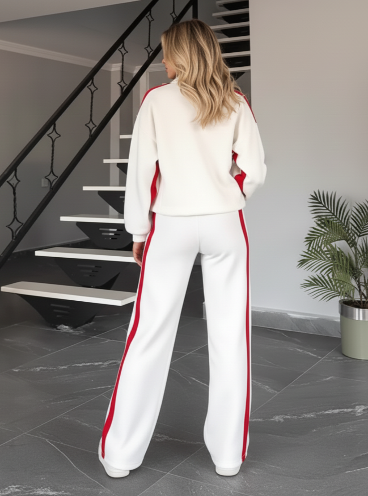Woman in a white outfit with red stripes standing in a modern interior setting.