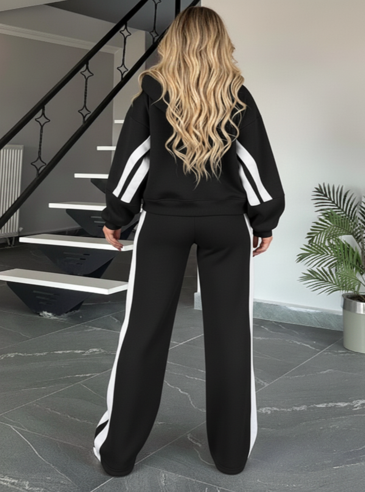 Person wearing a black tracksuit with white stripes in a home setting.