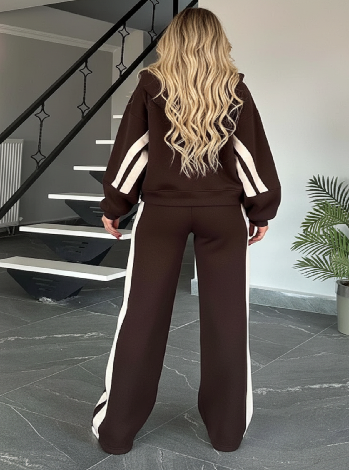Person wearing a brown tracksuit with white stripes in a modern interior setting.