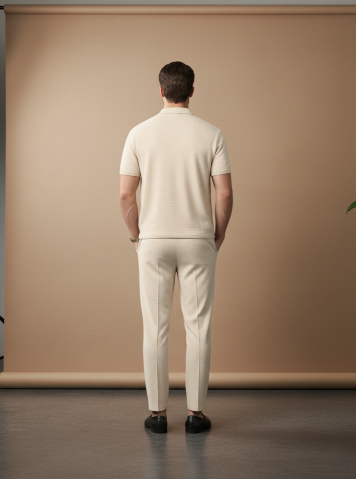 Man wearing a white outfit standing in front of a beige backdrop in a studio setting.