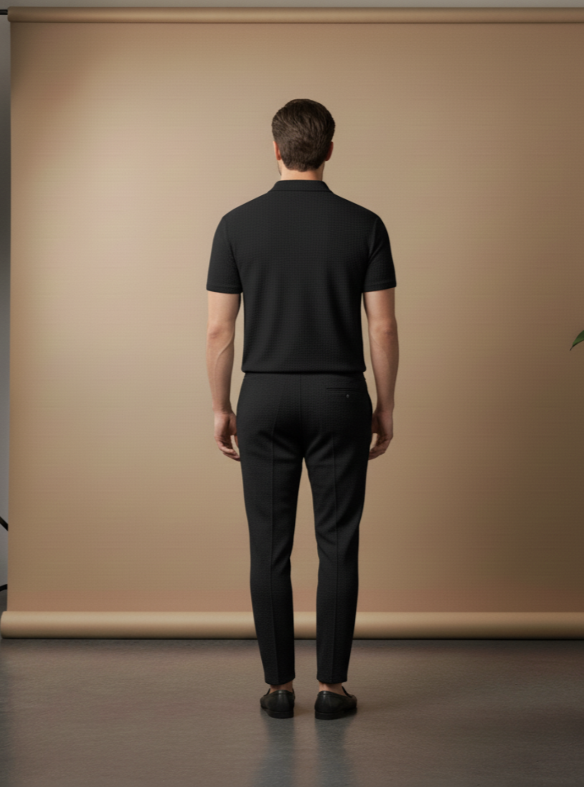 Man wearing a black outfit standing in front of a beige backdrop in a studio setting.