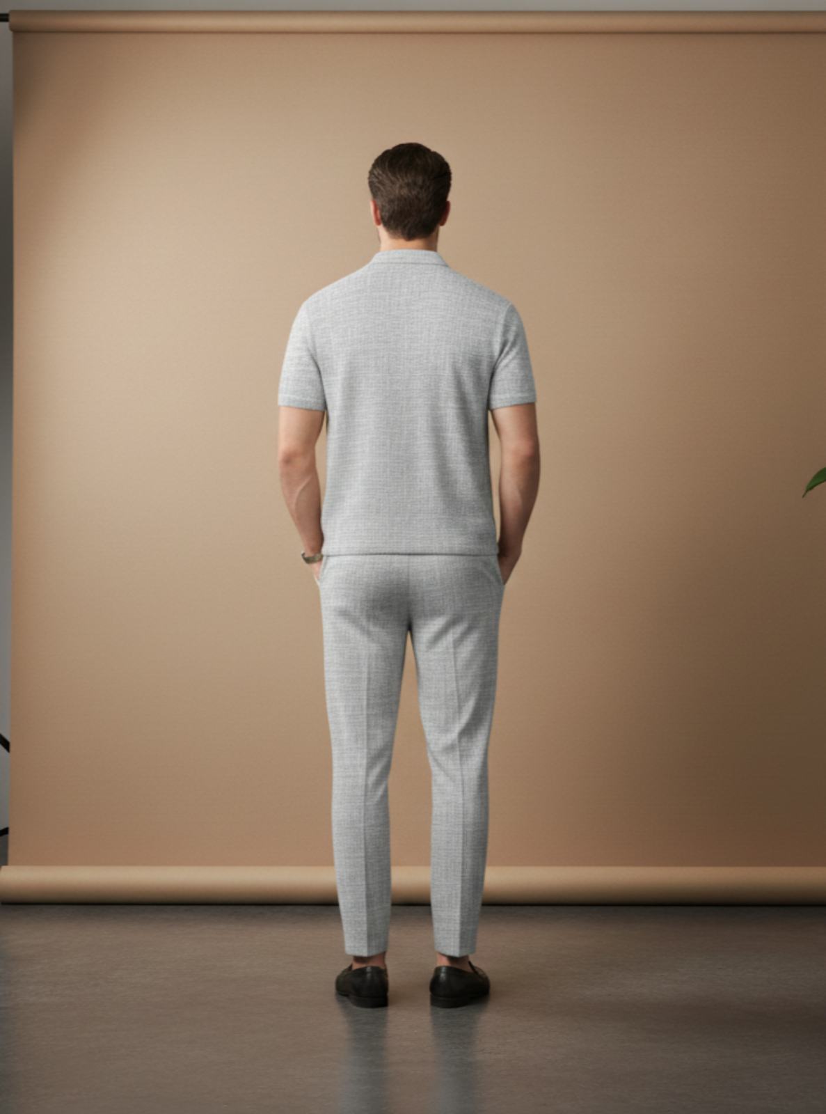 Man wearing a light gray outfit standing in front of a beige backdrop in a studio setting.