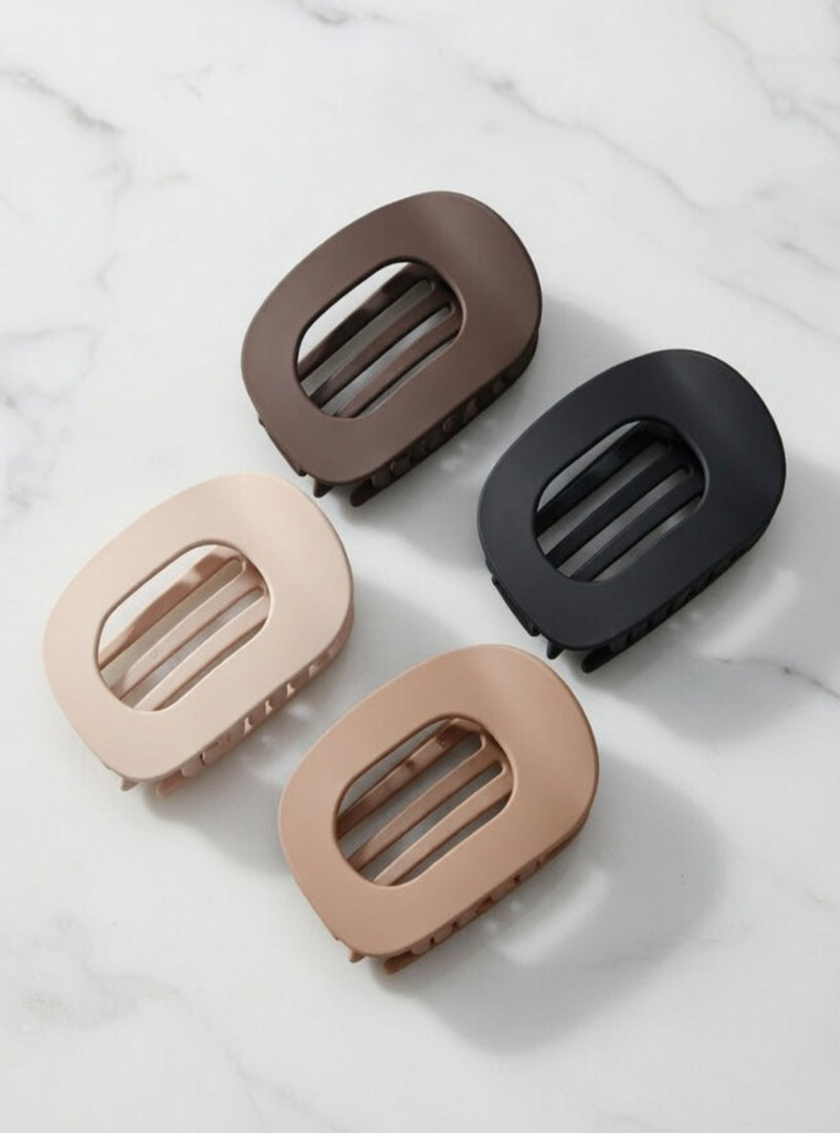 Four hair clips in brown, black, and beige on a marble surface