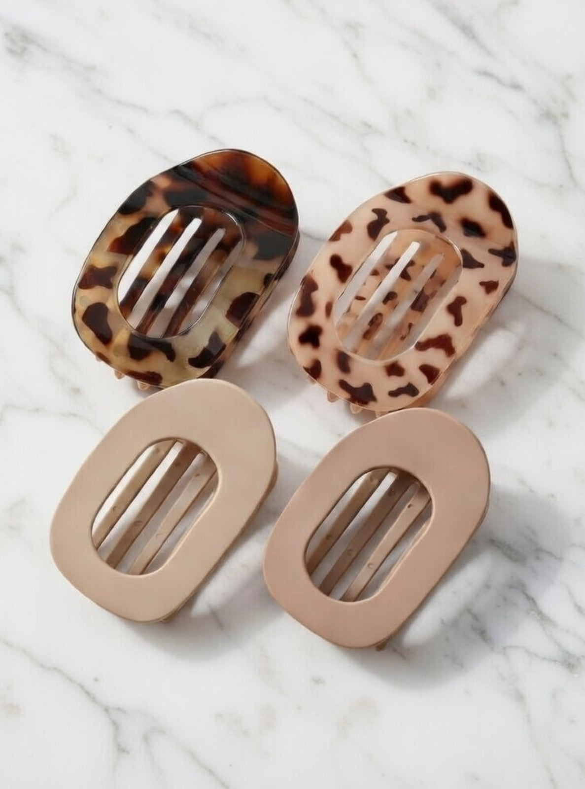 Two tortoiseshell patterned hair clips and two beige hair clips on a marble background