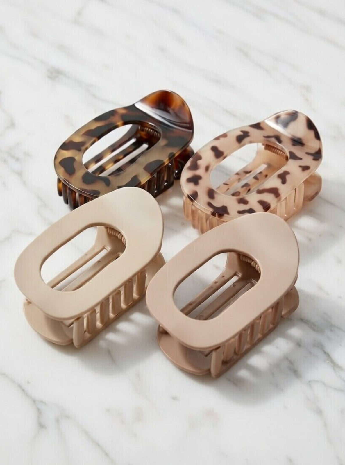 Four hair clips with tortoiseshell and beige patterns on a marble surface