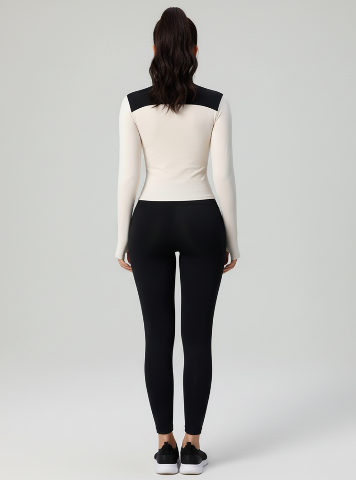 Person wearing a white long-sleeve top with black accents and black leggings on a light gray background