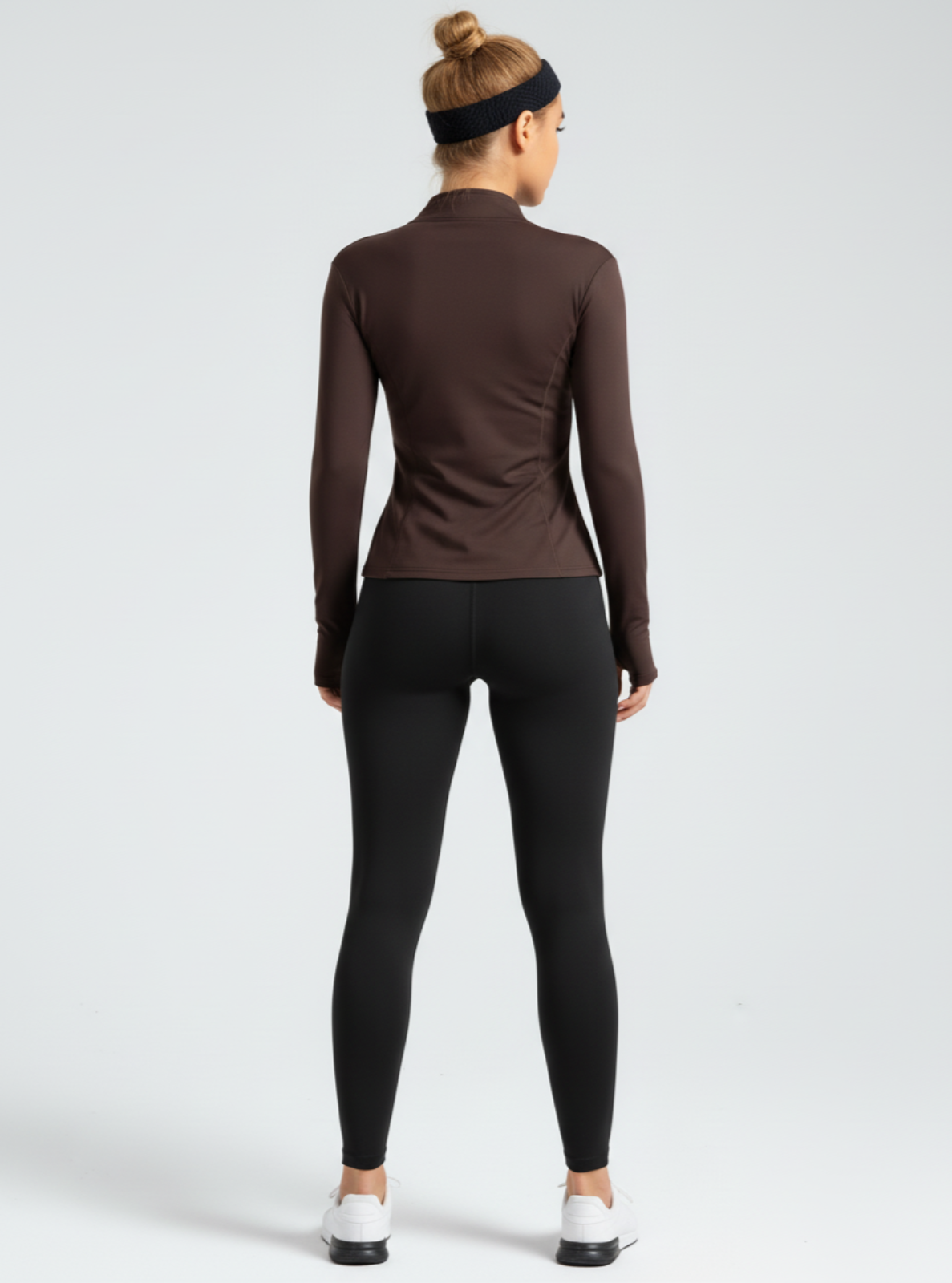 Person wearing a brown long-sleeve top and black leggings on a white background