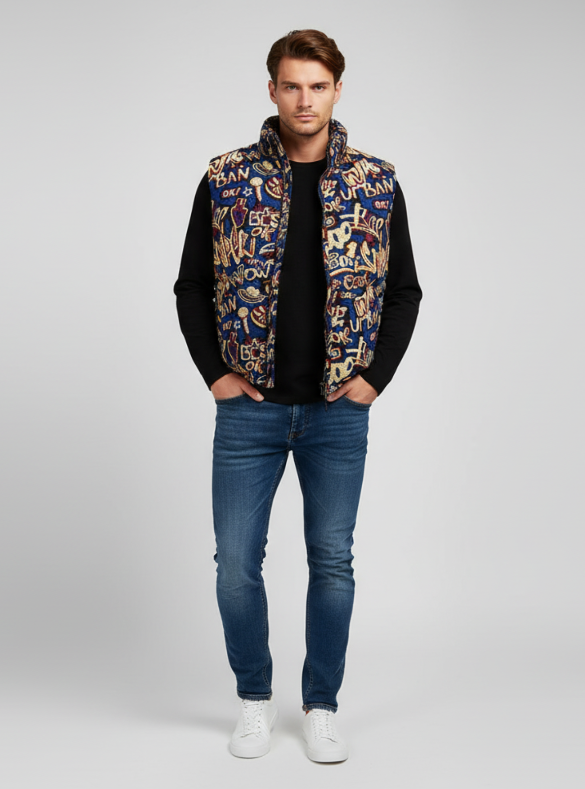 Man wearing a patterned vest over a black shirt with blue jeans on a gray background