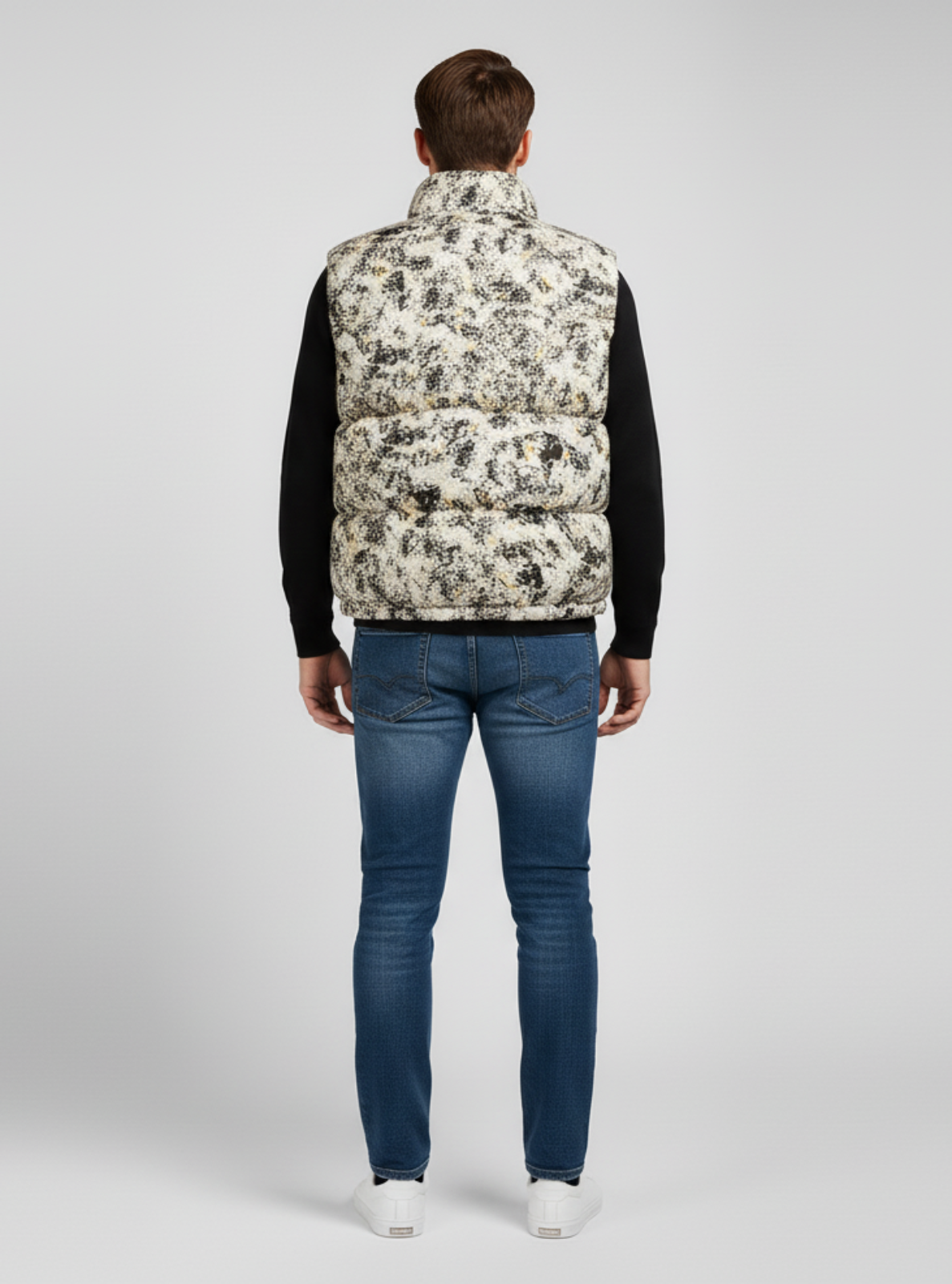 Person wearing a patterned puffer vest and blue jeans on a gray background