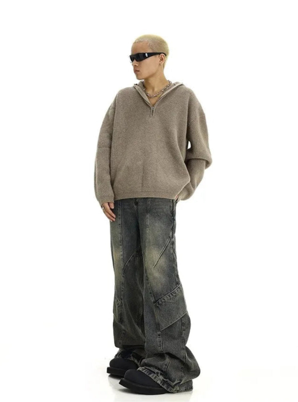 man wearing a beige sweater and dark jeans on a white background