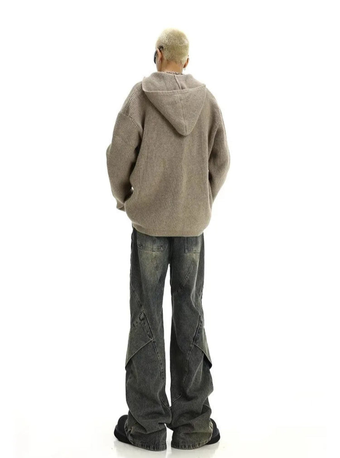 Person wearing a beige hoodie and dark jeans on a white background