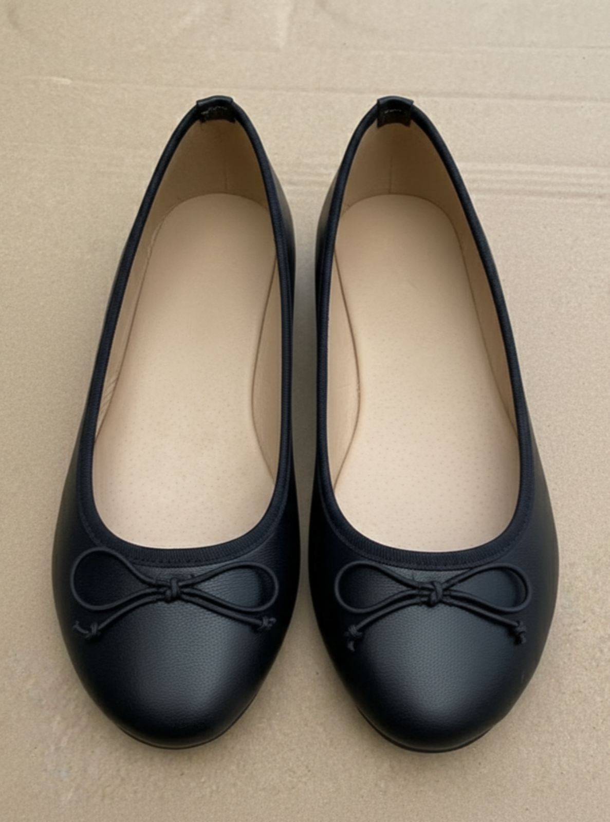 Pair of black ballet flats with bows on a beige background