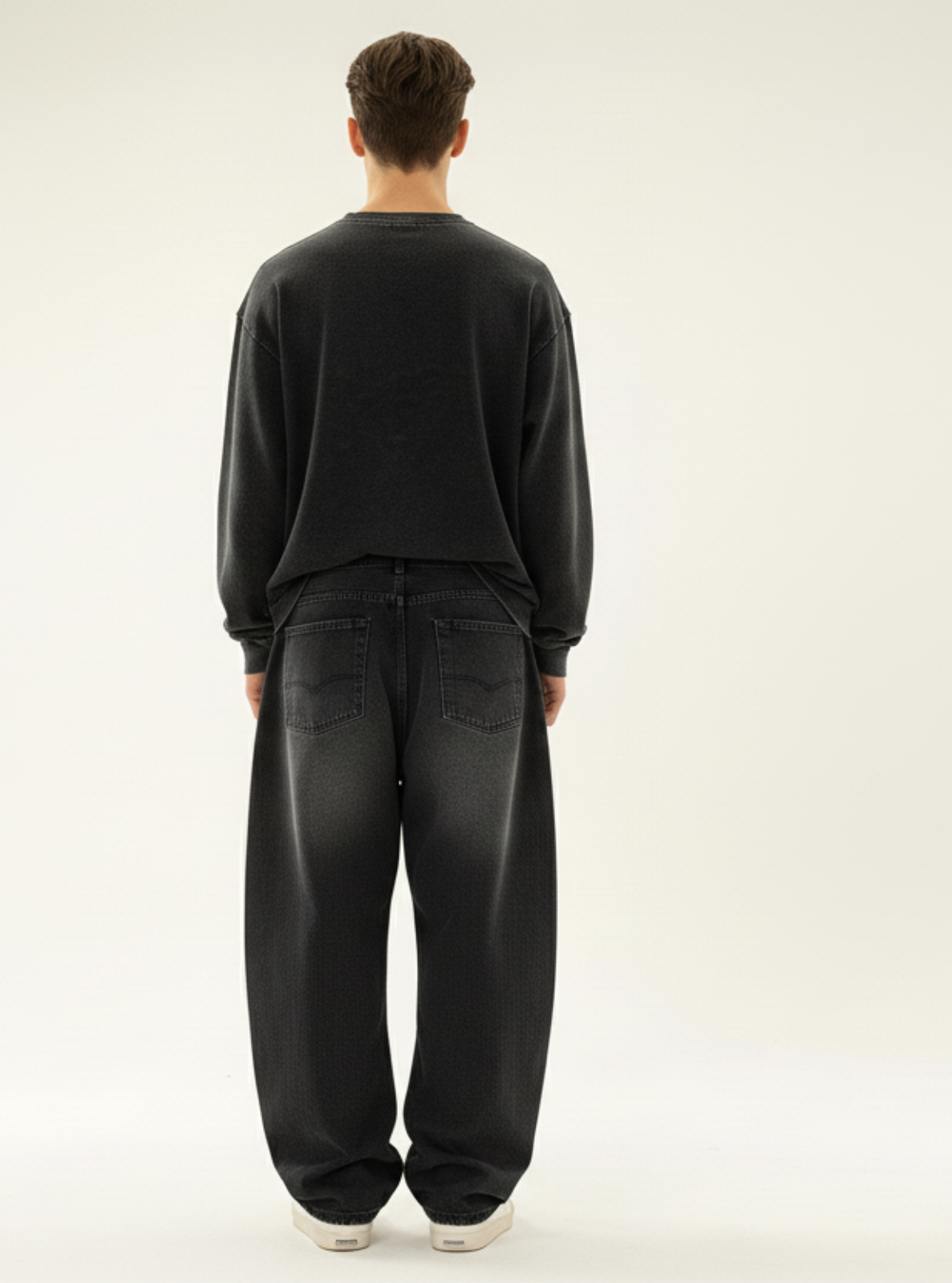 Person wearing a black sweater and jeans standing against a white background