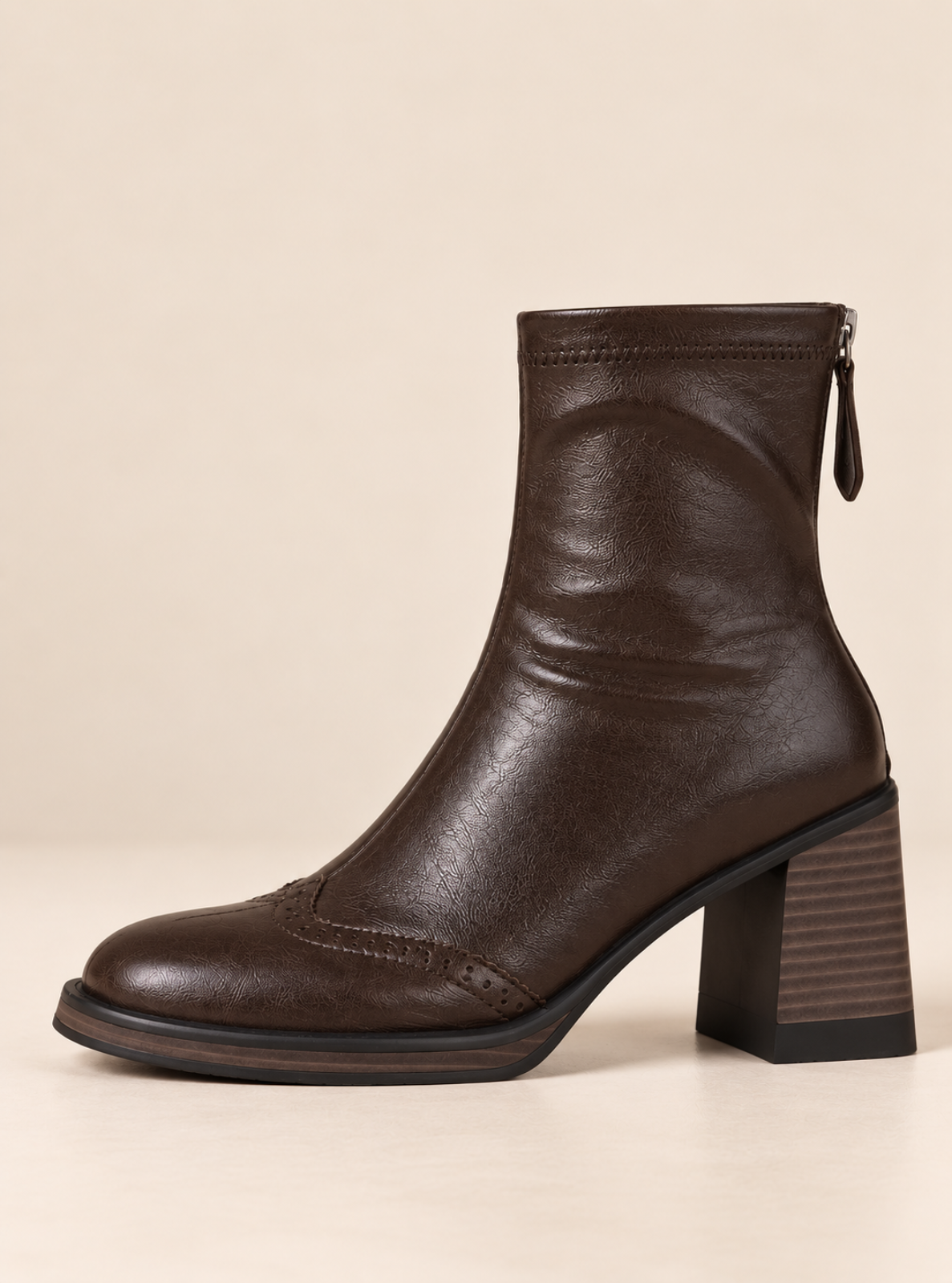 A dark brown leather ankle boot with a chunky block heel, a zippered back, and a low-cut toe, shown against a solid beige background.