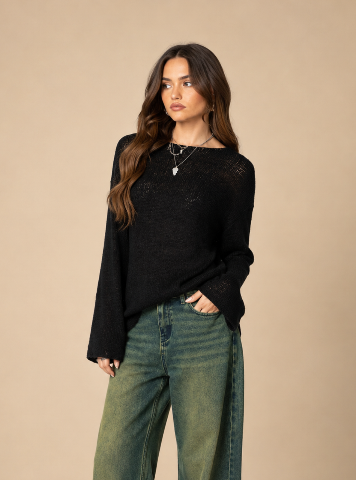 A woman modeling a black long-sleeve knit top and wide-leg green jeans against a solid beige studio background.