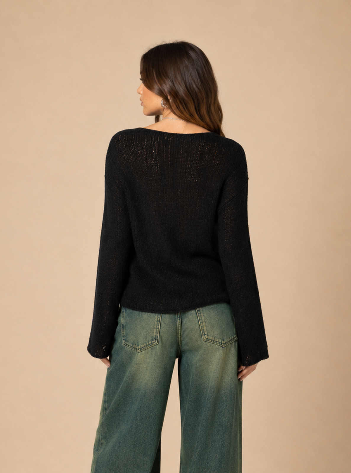 A woman shown from the back wearing a black long-sleeve knit top and wide-leg green jeans, standing against a plain beige studio background.