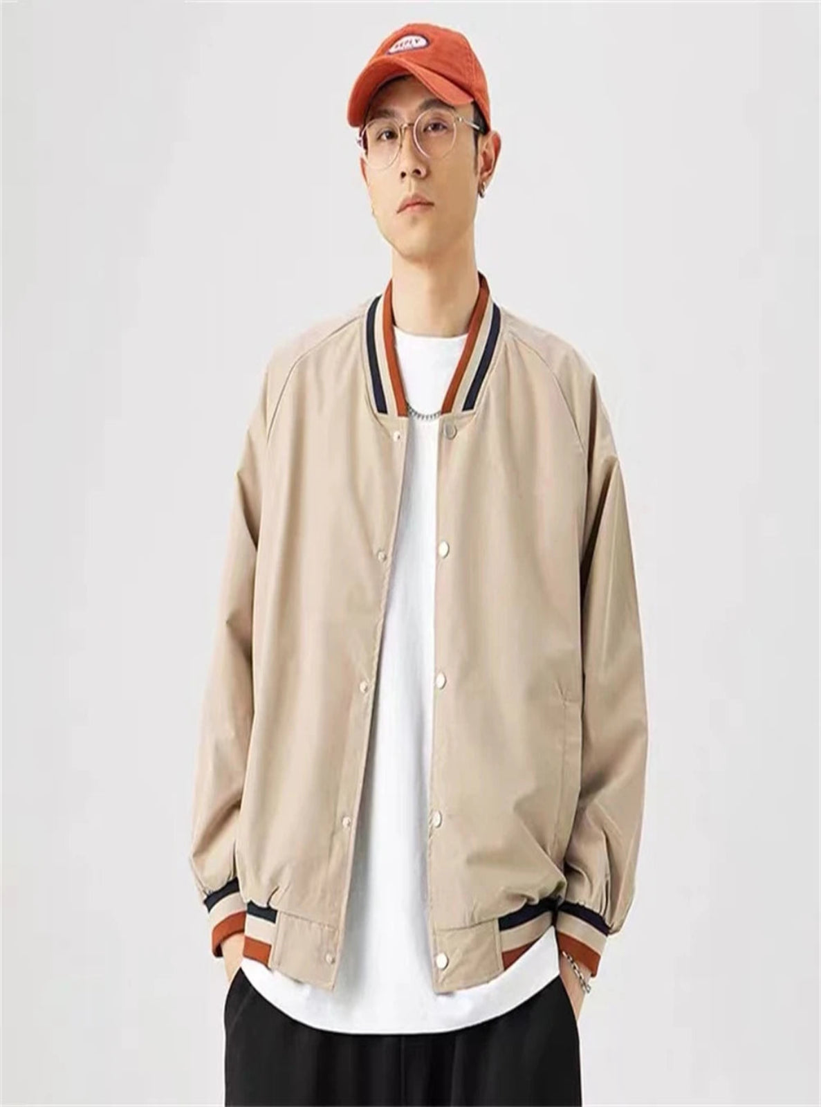 Person wearing a beige bomber jacket, white shirt, and red cap on a light gray background