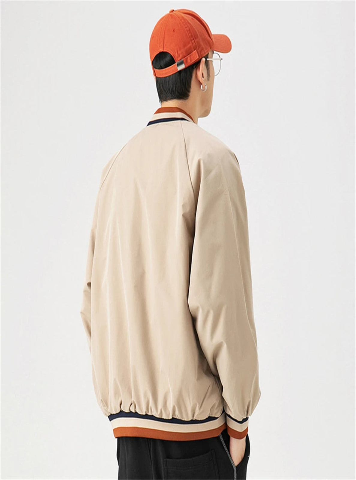 Person wearing a beige bomber jacket and orange cap on a light gray background