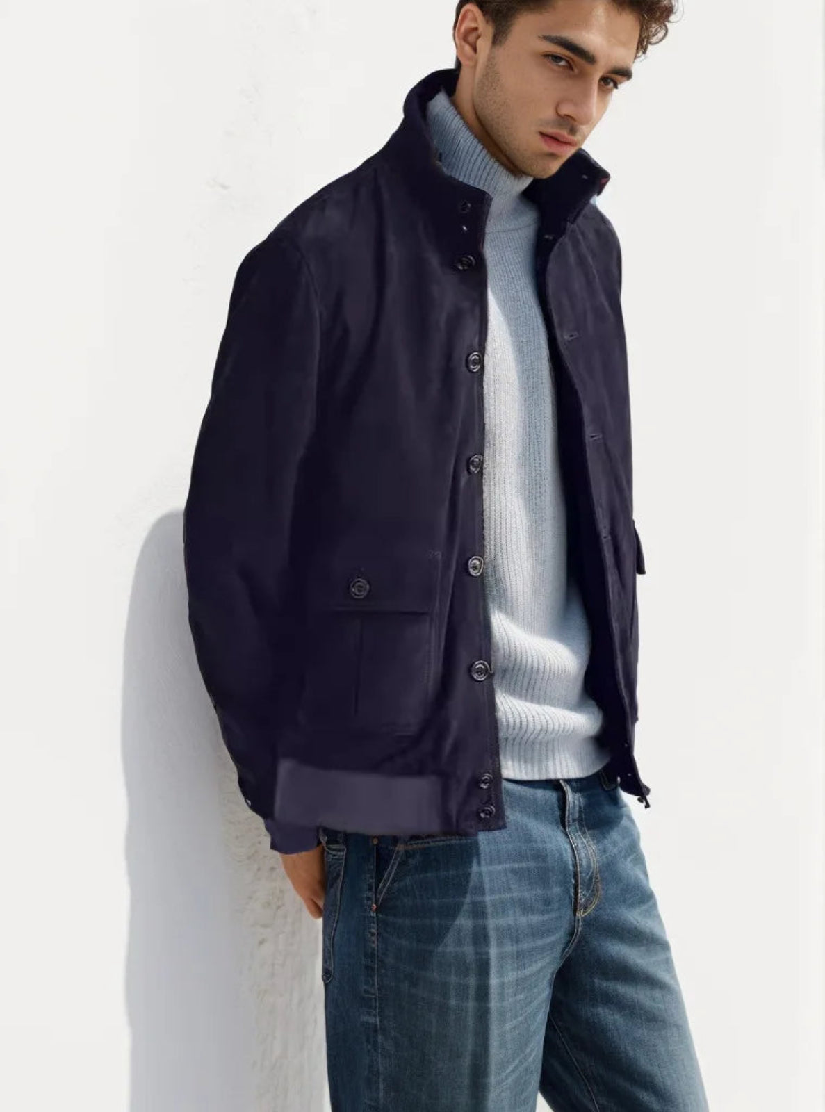 Man wearing a navy jacket over a light gray sweater and blue jeans against a white background