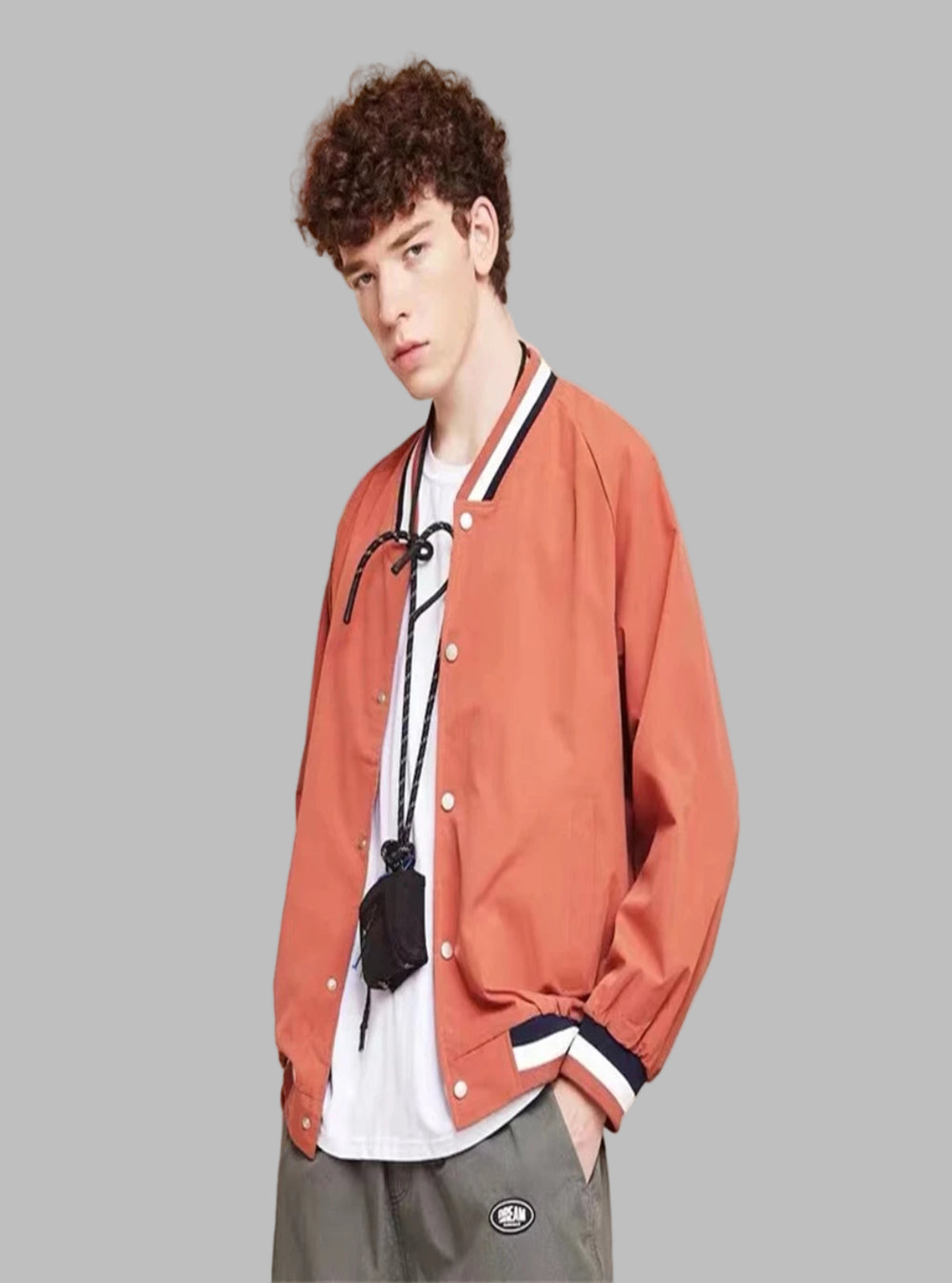 Person wearing an orange jacket over a white shirt with a black bag, standing against a beige background