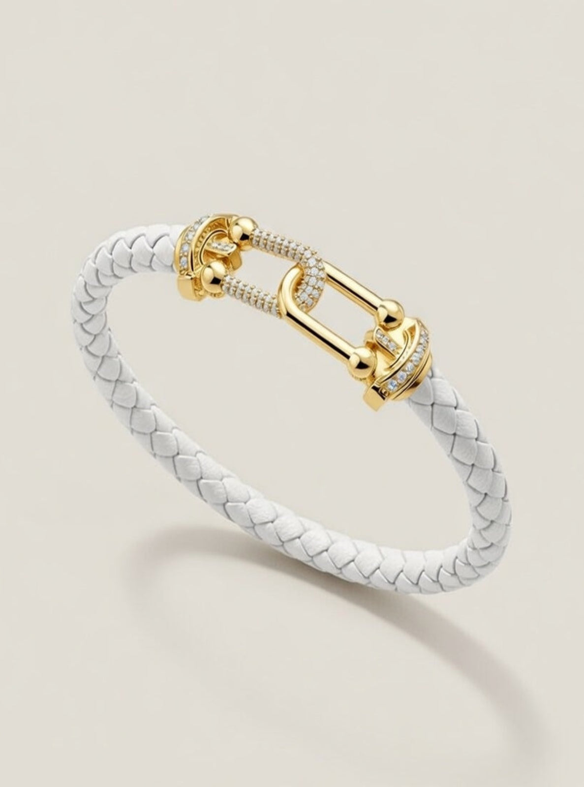 Gold clasp bracelet with white braided band on beige background