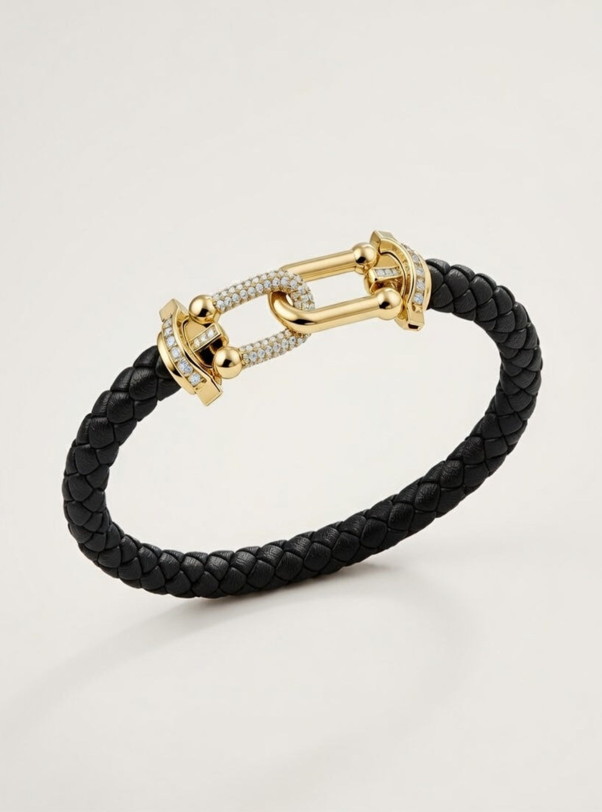 Black braided leather bracelet with gold clasp on a light gray background