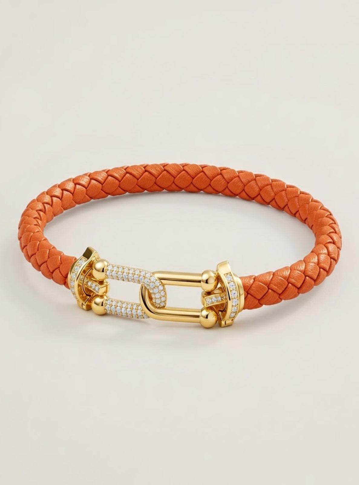 Orange braided leather bracelet with a gold clasp on a light beige background