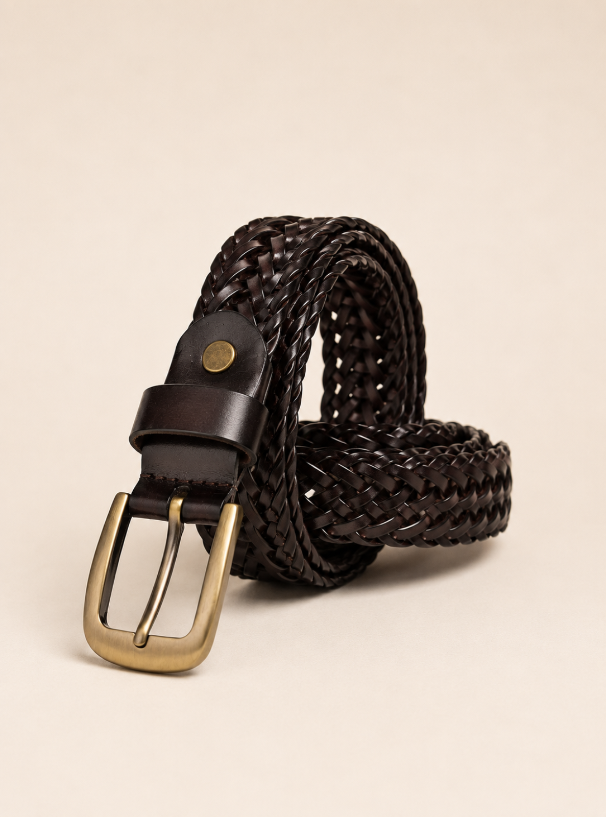 A dark brown braided leather belt with a polished gold-tone buckle, coiled on a light beige background.