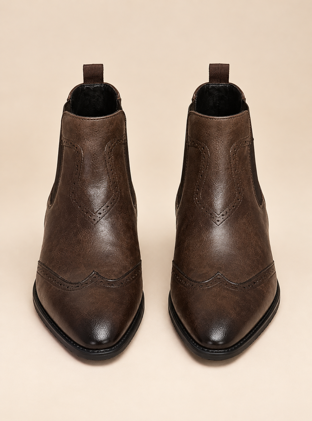 A pair of dark brown leather ankle boots with pointed toes, decorative brogue-style stitching, and elastic side gore panels, shown against a solid beige background.