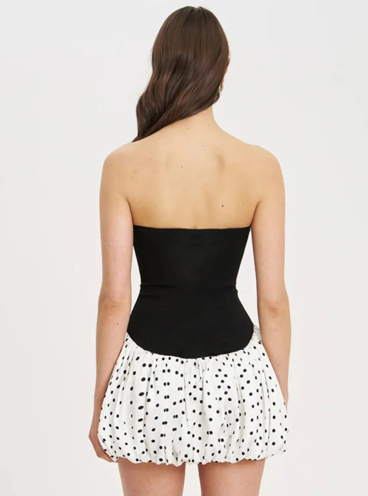 Woman wearing a black strapless top and white polka dot skirt on a light gray background