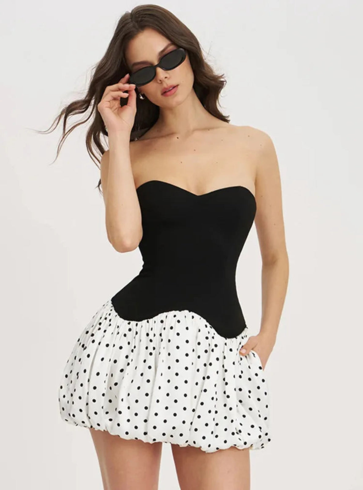 Woman wearing a black strapless top and polka dot skirt on a white background