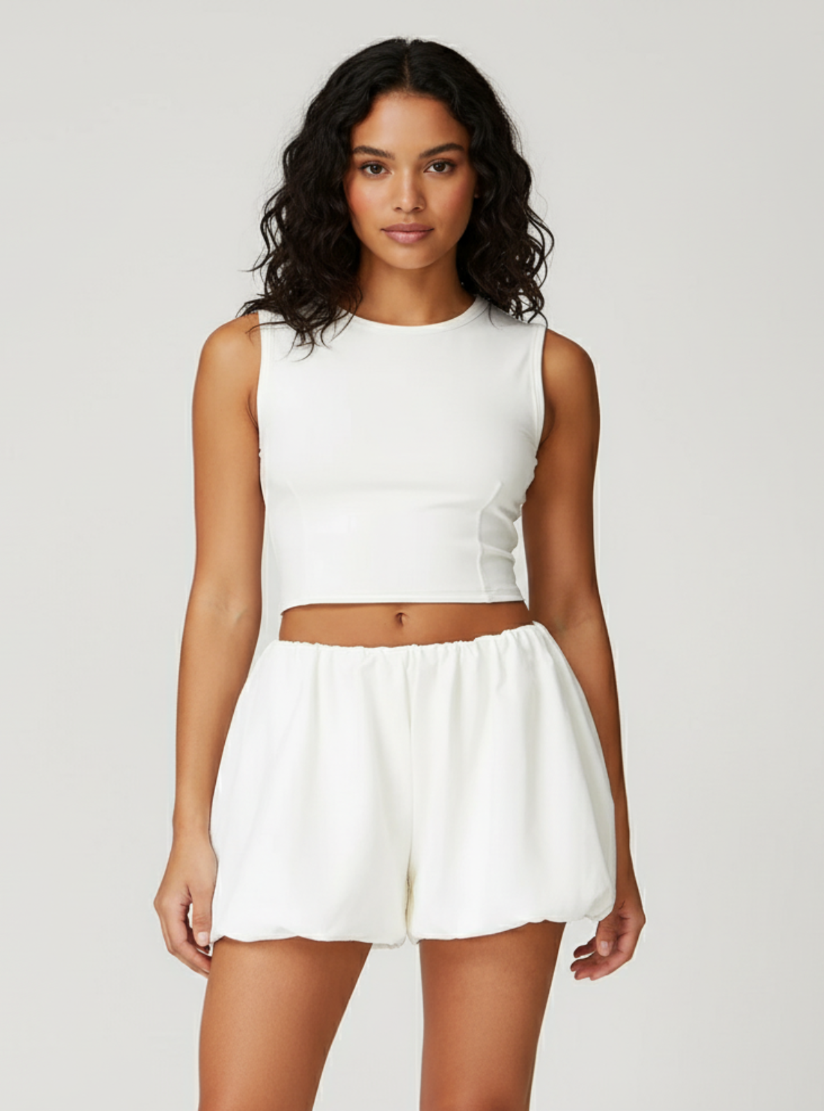 Woman wearing a white sleeveless top and shorts on a plain background