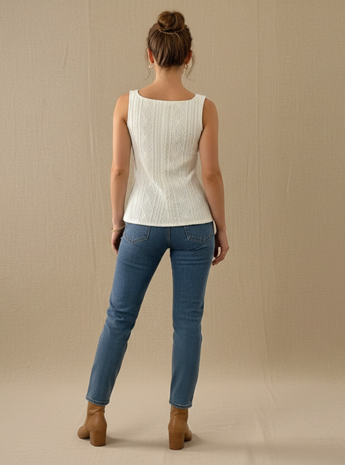 Woman wearing a white sleeveless top and blue jeans against a beige background