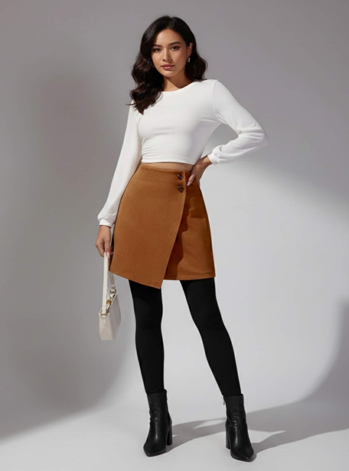 Woman wearing a white top, brown skirt, black tights, and black boots on a gray background