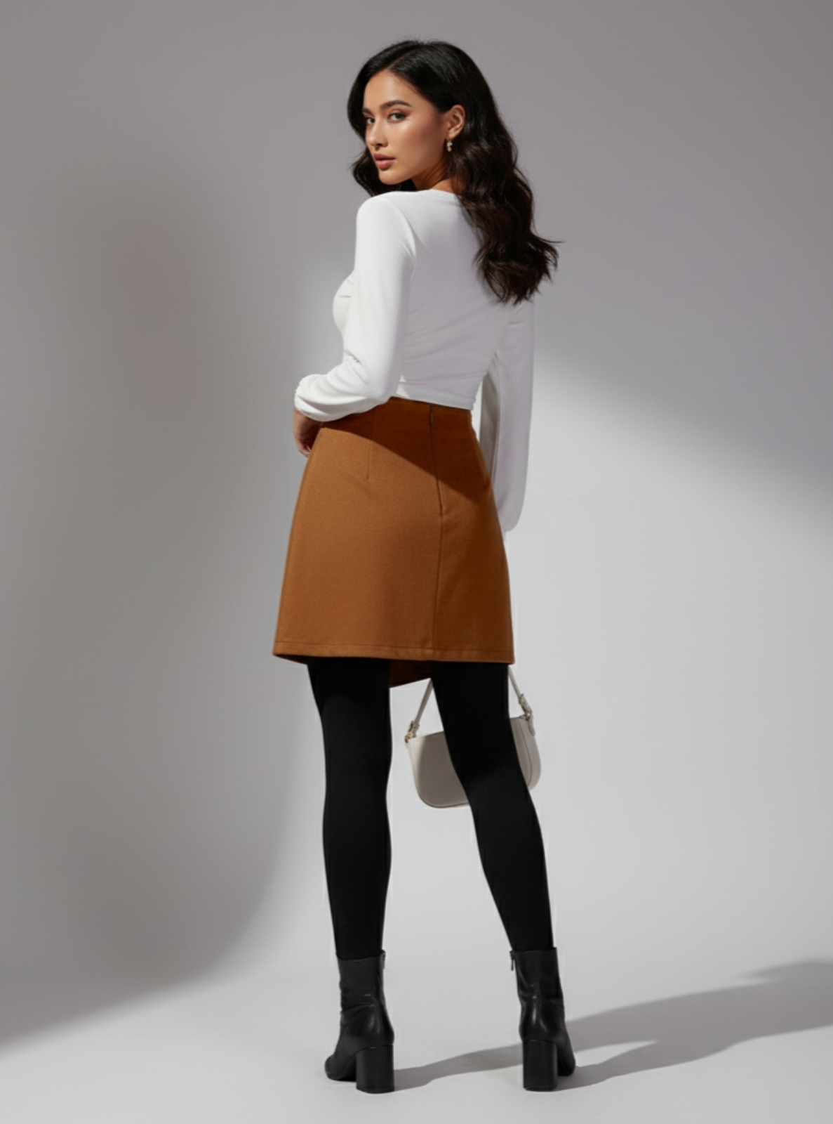 Woman wearing a white blouse, brown skirt, black tights, and black boots on a gray background