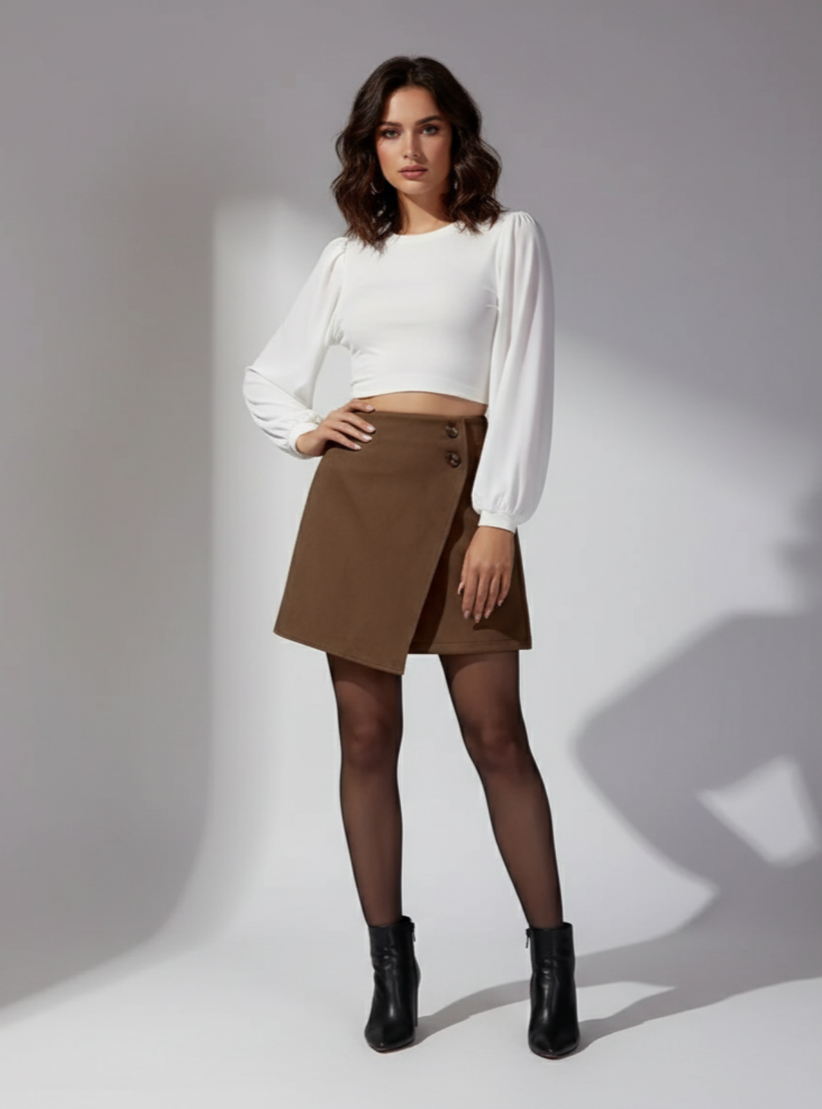 Woman wearing a white blouse, brown skirt, and black boots on a gray background