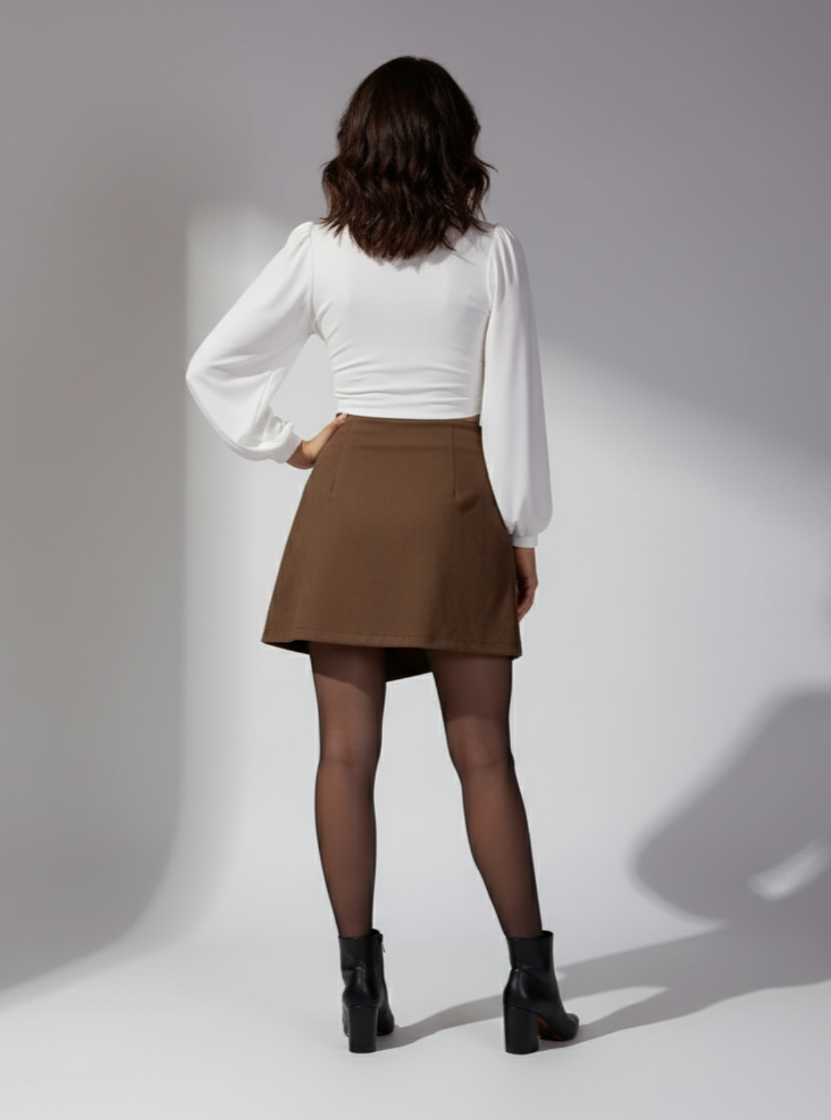 Woman wearing a white blouse and brown skirt against a gray background