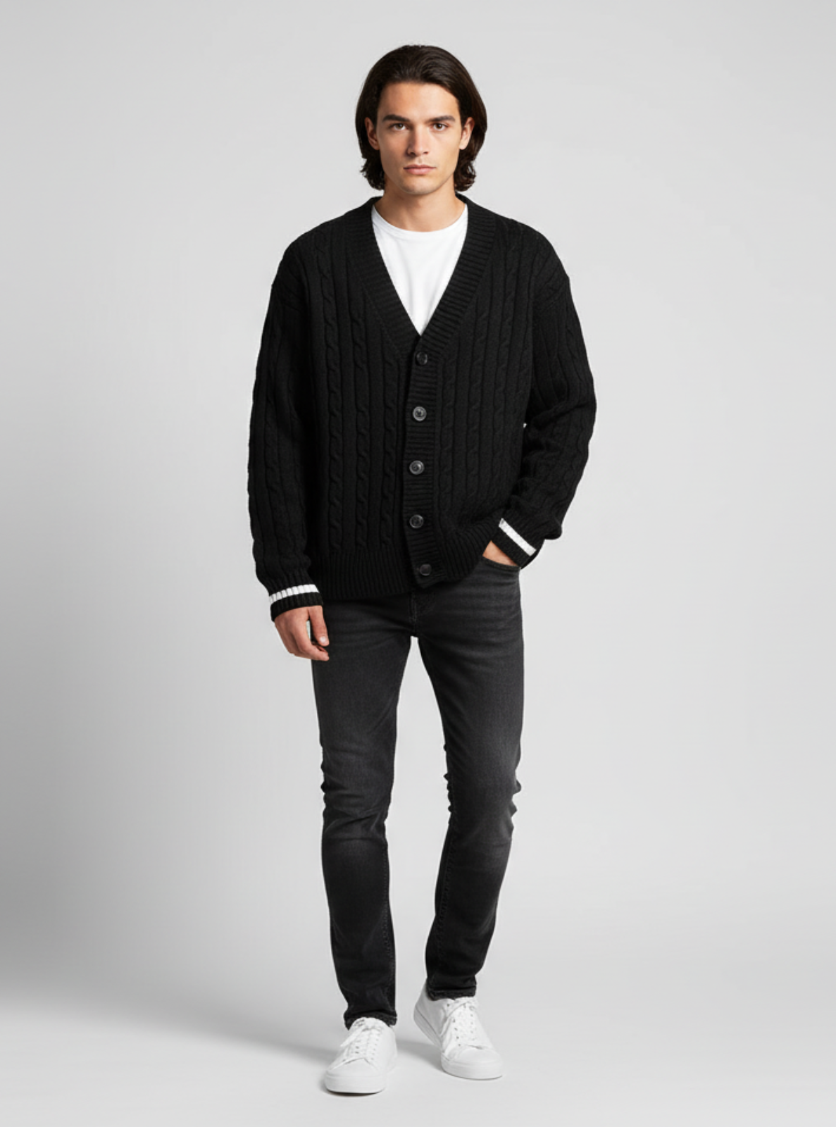 Man wearing a black cardigan, white shirt, and dark jeans on a light gray background