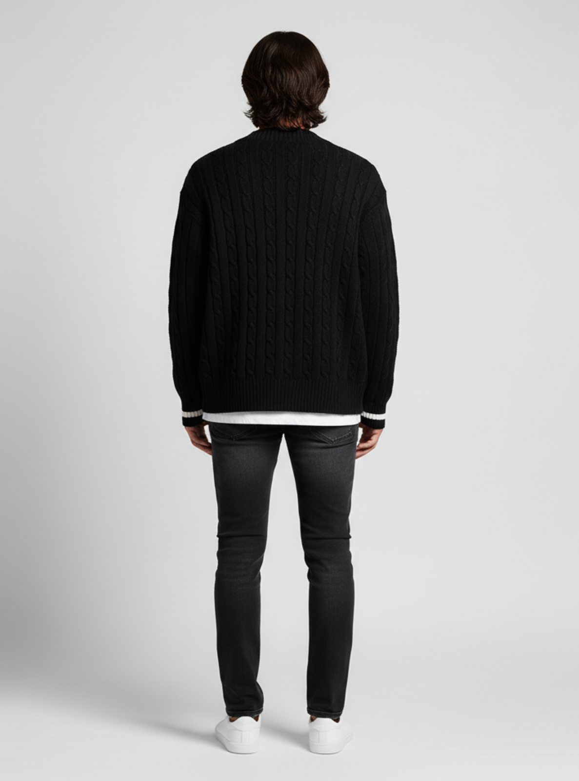 Person wearing a black sweater and dark jeans on a light gray background