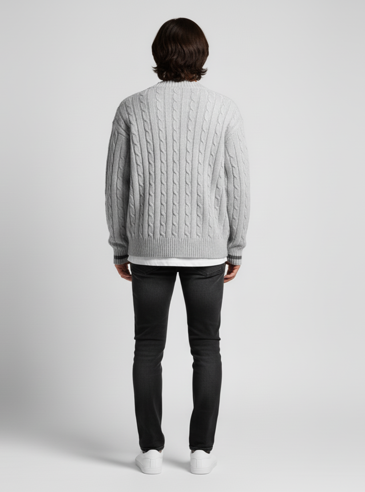 Person wearing a gray cable knit sweater and black pants on a light gray background