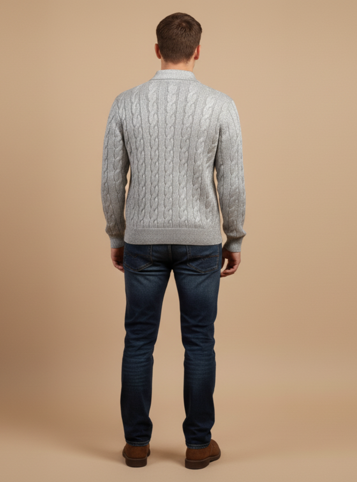 Man wearing a gray cable knit sweater and dark jeans on a beige background