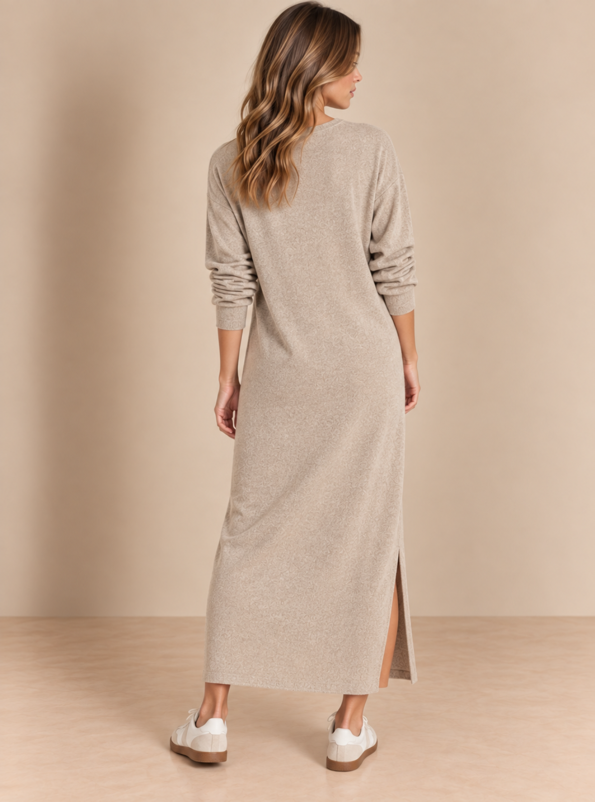 A woman viewed from the back wearing a long-sleeve knit midi dress in a light taupe-beige color, paired with white sneakers, set against a solid beige studio background.