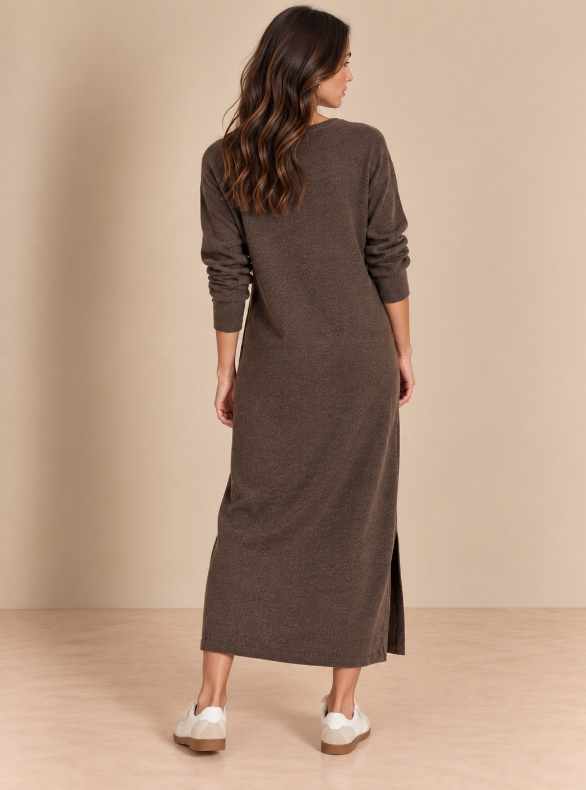 A woman shown from the back wearing a long-sleeve brown knit midi dress with a side slit, paired with white sneakers, against a beige studio backdrop.