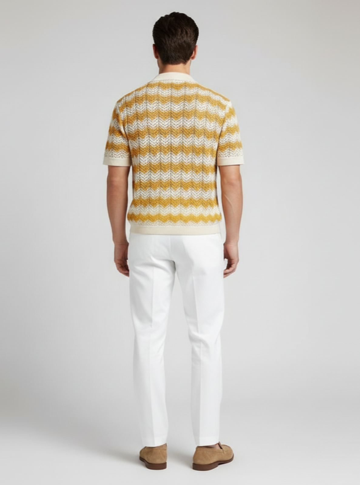 Person wearing a yellow and white striped sweater and white pants on a plain background