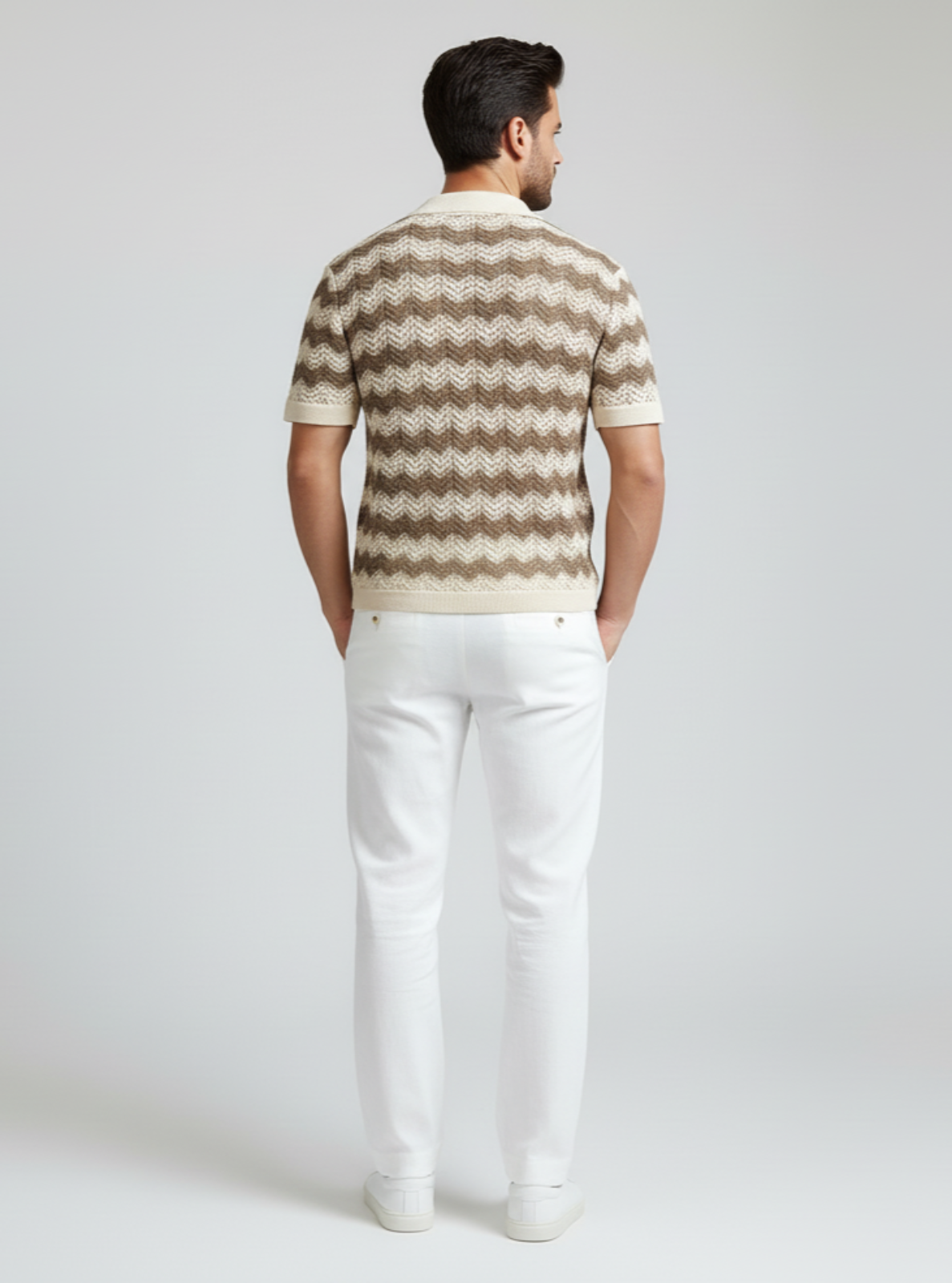 Man wearing a patterned shirt and white pants on a plain background